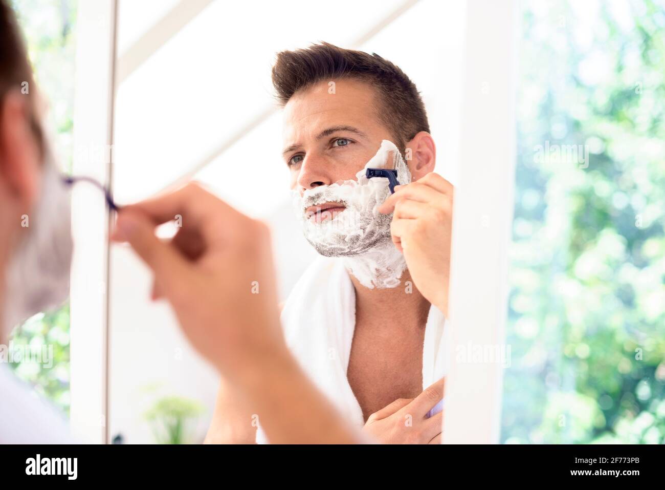 Un bell'uomo con un asciugamano intorno al collo utilizzando la schiuma da  barba mentre si scula davanti allo specchio del bagno Foto stock - Alamy
