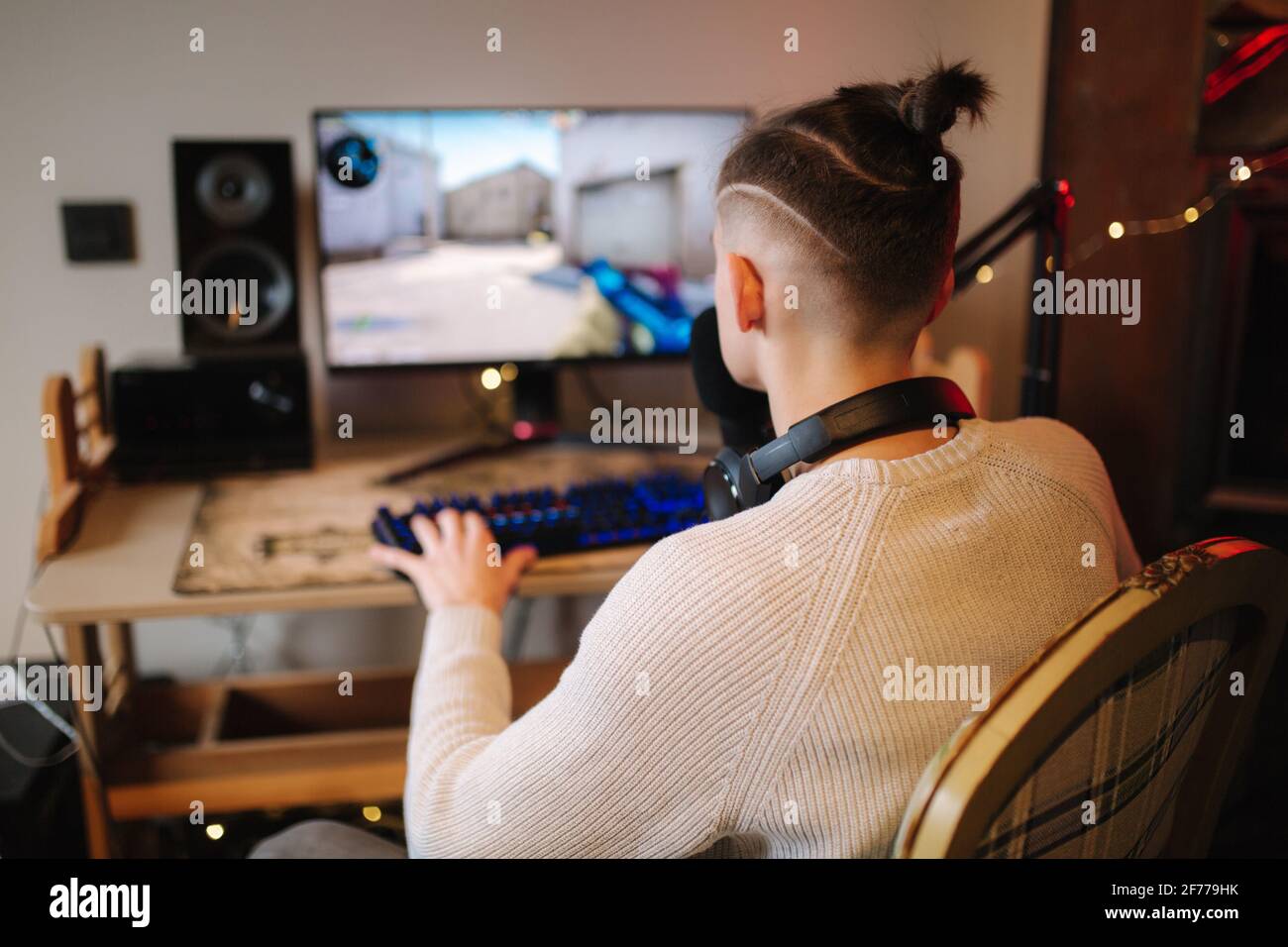 Uomini che giocano a videogame online a casa utilizzando un potente computer. Snellire l'uomo utilizzando microfono, tastiera e mouse professionali in studio di casa di gioco. Indietro Foto Stock