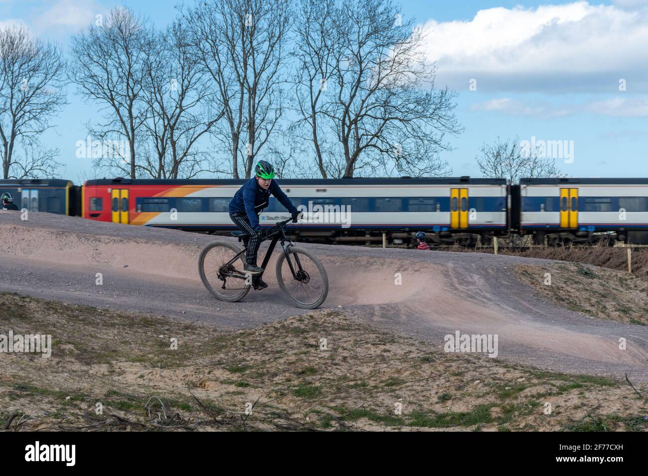 Mountain e BMX pista ciclabile a Edenbrook Country Park con ciclista a cavallo, e un treno sullo sfondo, Fleet, Hampshire, Regno Unito Foto Stock