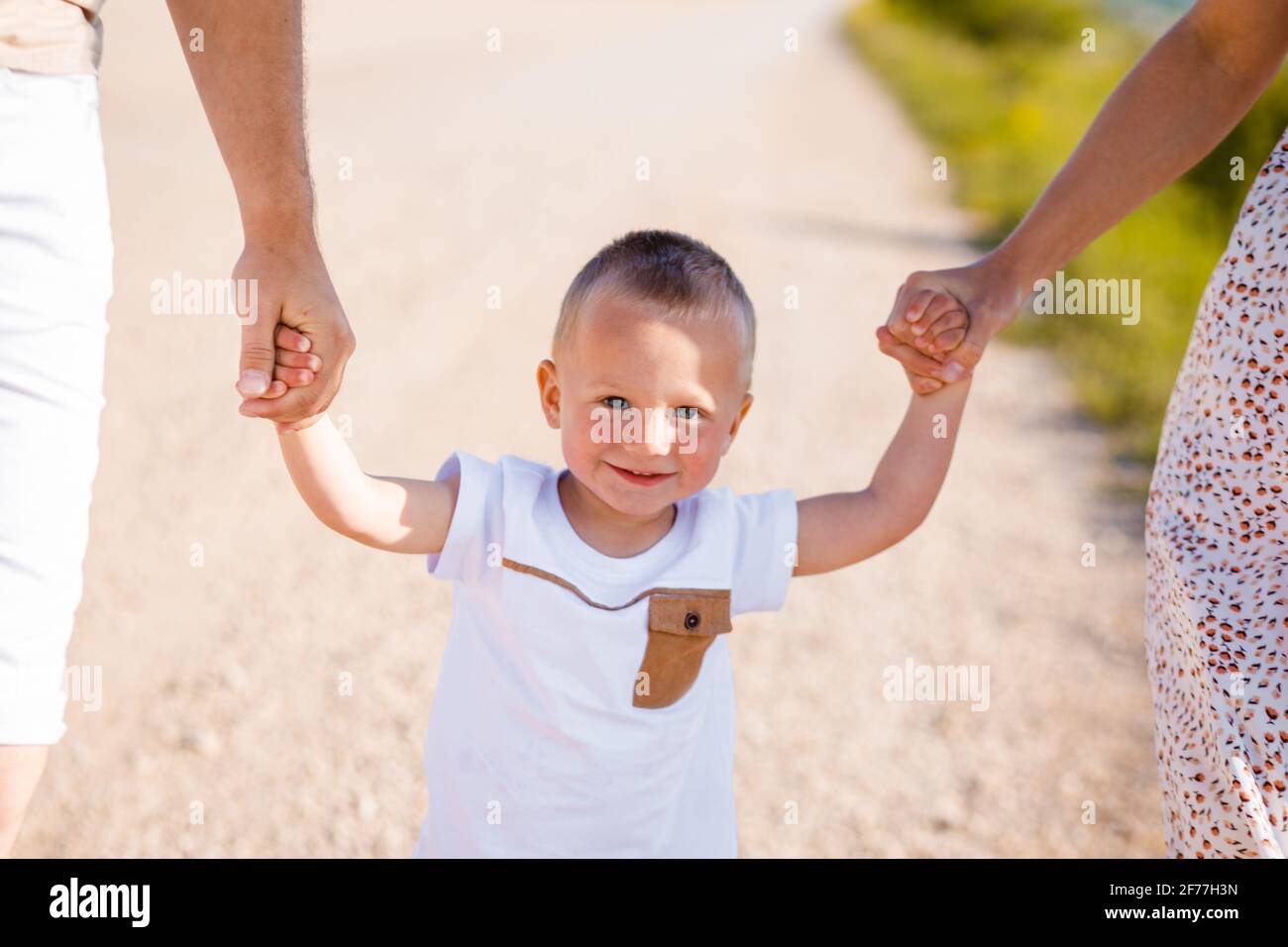 Felice infanzia di un bambino con mamma e papà. Il bambino tiene la mano dei genitori. Foto Stock