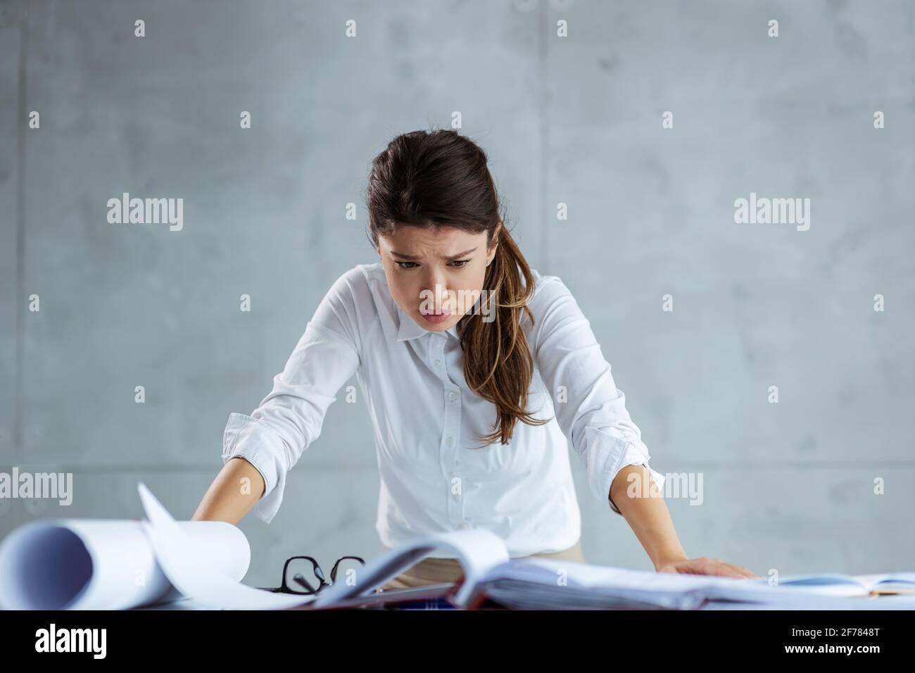 Impegnata architetto femminile che si appoggia alla scrivania e guarda progetti e documenti. Foto Stock