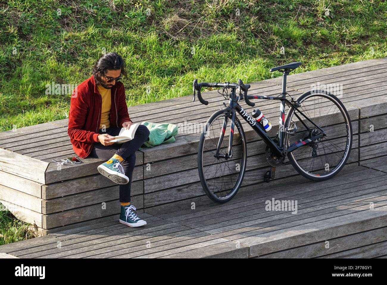 Giovane uomo seduto e leggere libro in un parco in molla Foto Stock