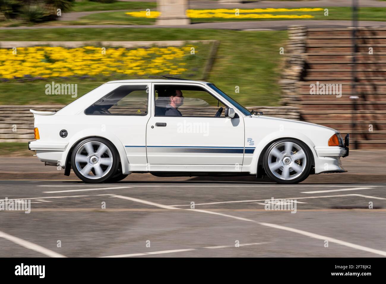 White Ford Escort RS Turbo a Southend on Sea, Essex, Regno Unito, passando accanto a fiori luminosi su Cliff Gardens. Auto stereotipata Essex Foto Stock