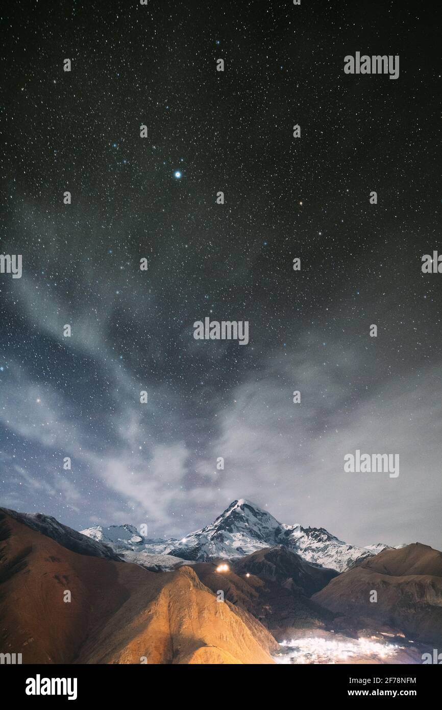 Stepantsminda, Georgia. Cielo stellato di notte con le stelle incandescenti sopra il picco del Monte Kazbek coperto di neve. Luce notturna. Bella georgiana Foto Stock