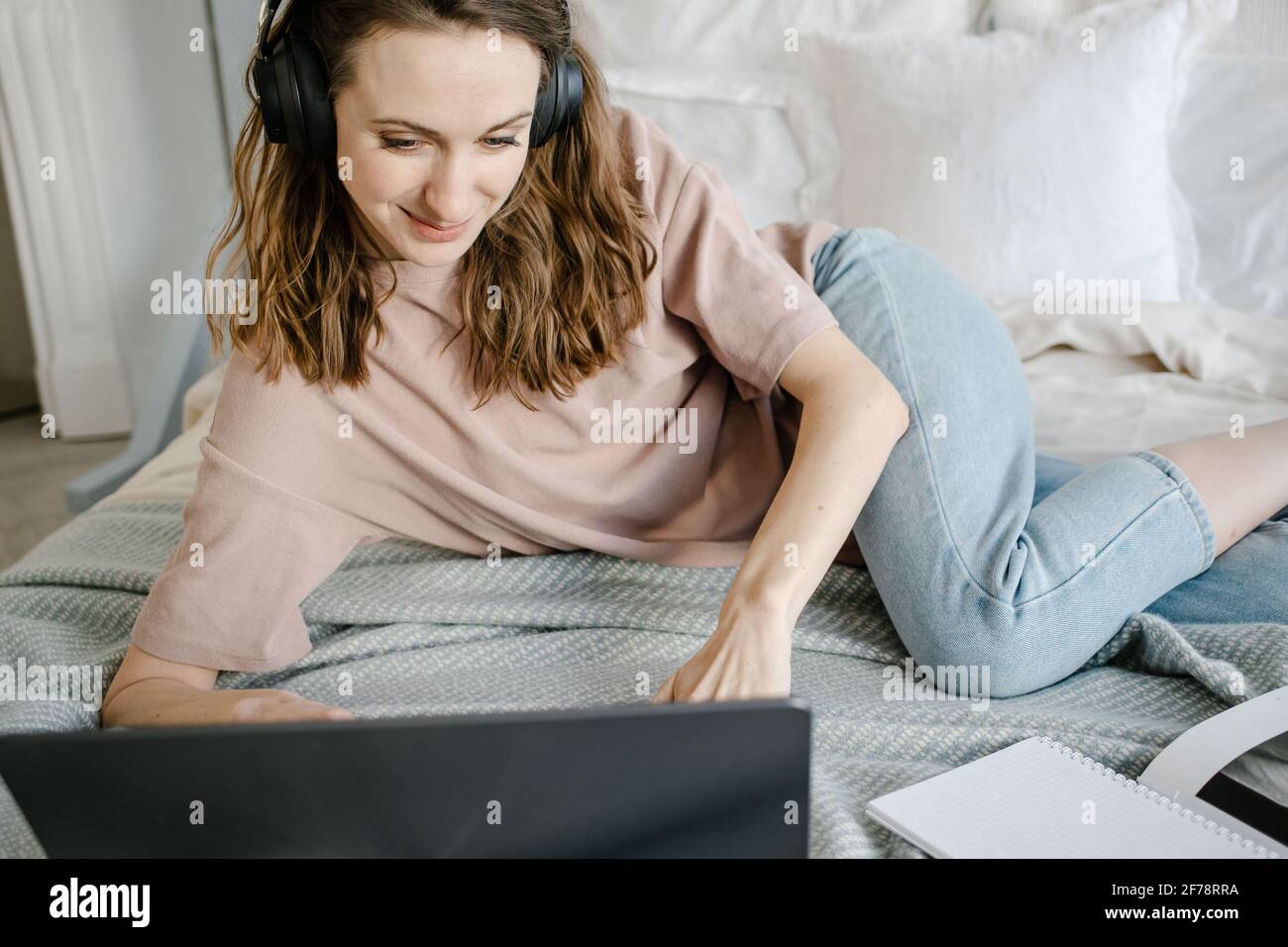 Distanza di apprendimento online istruzione e lavoro.felice donna in casual con le cuffie che lavorano su un computer portatile a distanza da casa a letto. Foto Stock