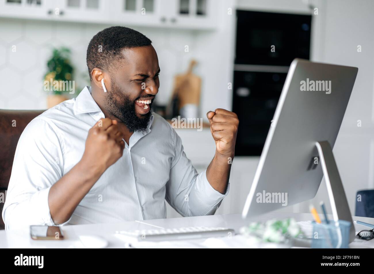 Felice fiducioso giovane freelancer afro-americano, manager o broker, vestito in abiti eleganti, lavorare a distanza, celebrare il successo, la vittoria o il buon profitto, gesturing con le mani, felicemente sorridente Foto Stock
