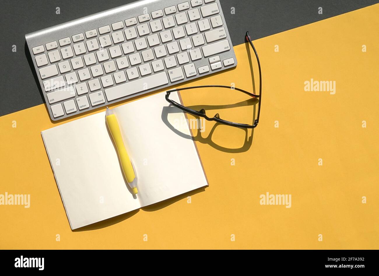 Tastiera wireless, occhiali da lettura e blocco note aperto su sfondo nero e giallo. Spazio di copia. Foto Stock