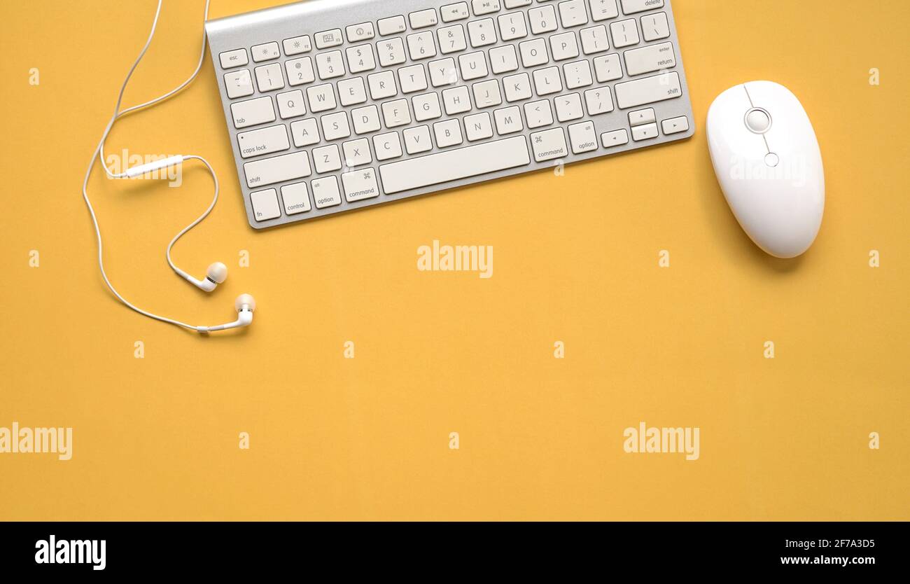 Vista dall'alto di tastiera, mouse e auricolari bianchi su un tavolo di sfondo giallo. Spazio di copia. Foto Stock