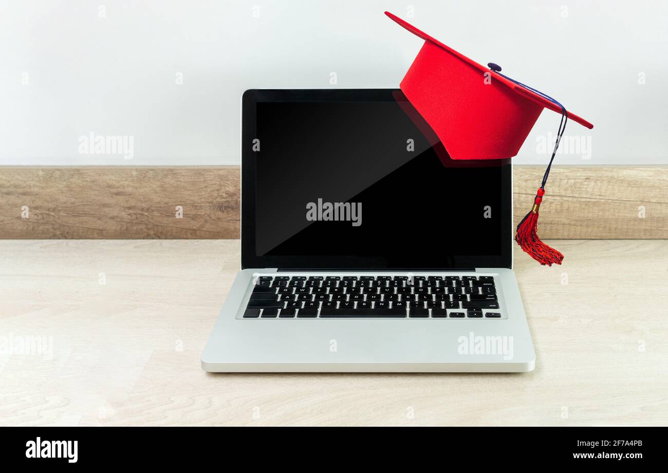 Concetto di formazione o laurea online con un computer portatile su un scrivania in legno con tappo rosso graduato Foto Stock