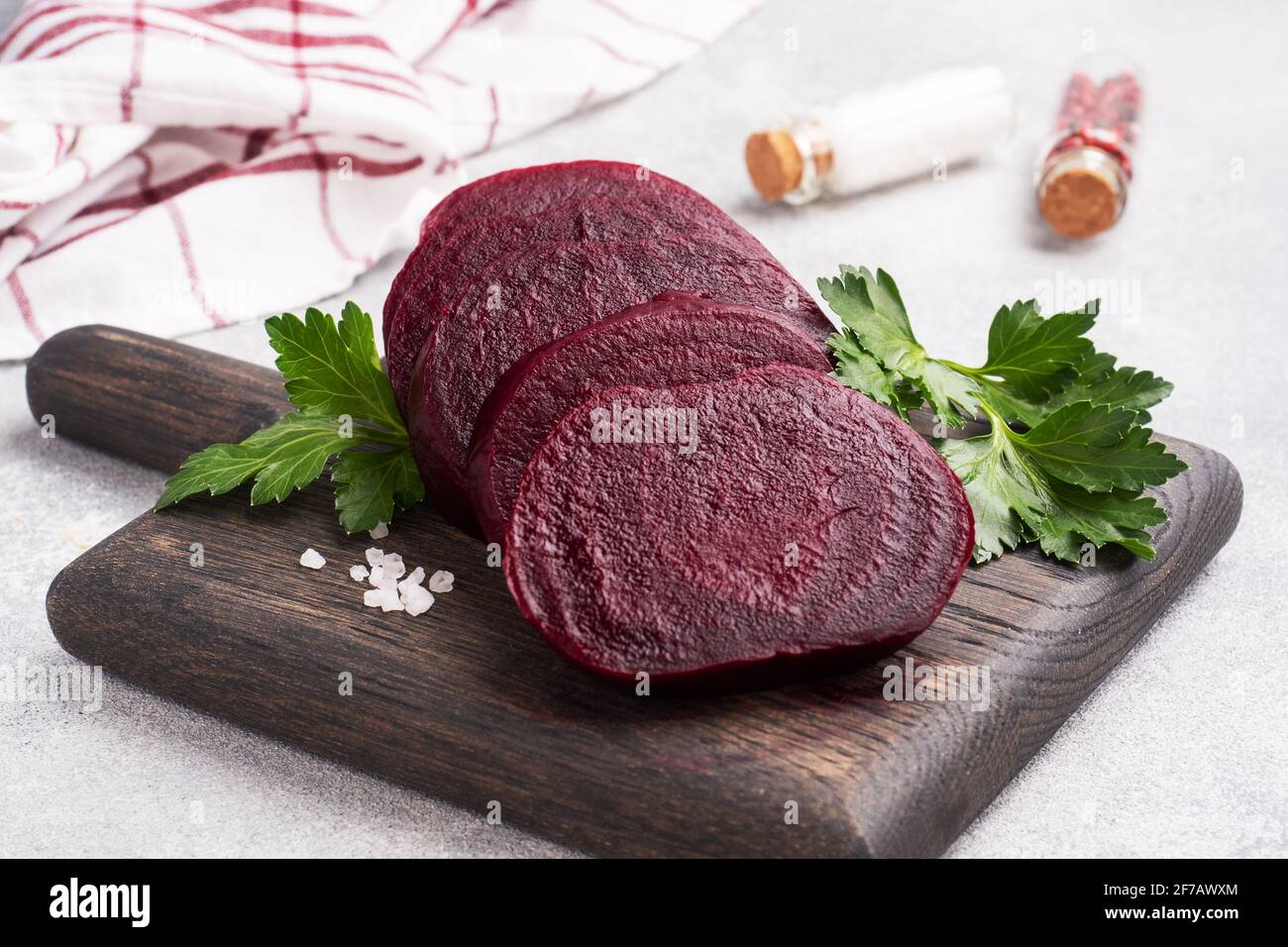 Fette di barbabietola bollita su un tagliere con foglie di prezzemolo su uno sfondo rustico di legno. Spazio di copia, Foto Stock