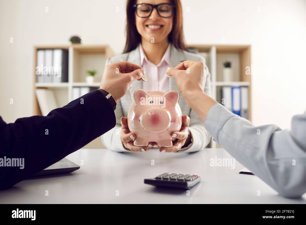 Mano di accoppiamento che mette la moneta in pink piggybank in consulente finanziario braccia Foto Stock