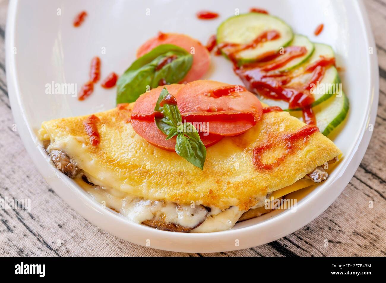 Una gustosa crepe saporita con melanzane, zucchine e pomodori su un piatto bianco, con decorazione a foglie di basilico Foto Stock