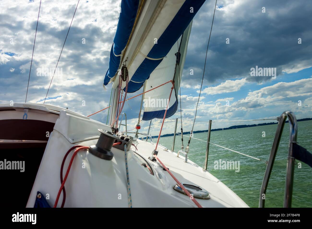 Barca a vela su un lago. Vela maestra stirata nel vento, con sole luminoso sullo sfondo. Naviga sopra il cielo blu. Vela nel vento Foto Stock