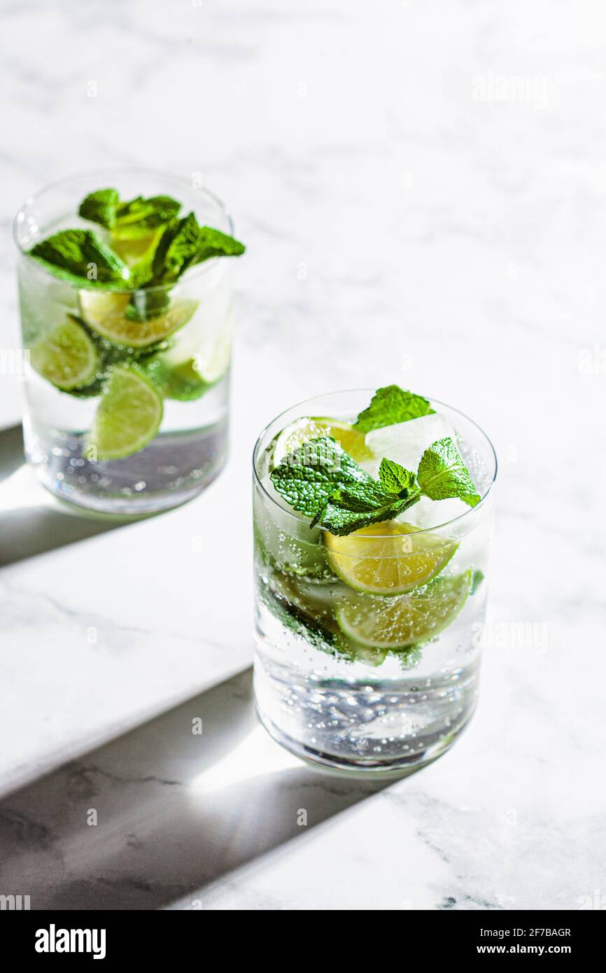 Cocktail Mojito con menta e lime in bicchieri, sfondo in marmo bianco. Bevanda rinfrescante con lime e menta in bicchieri. Foto Stock