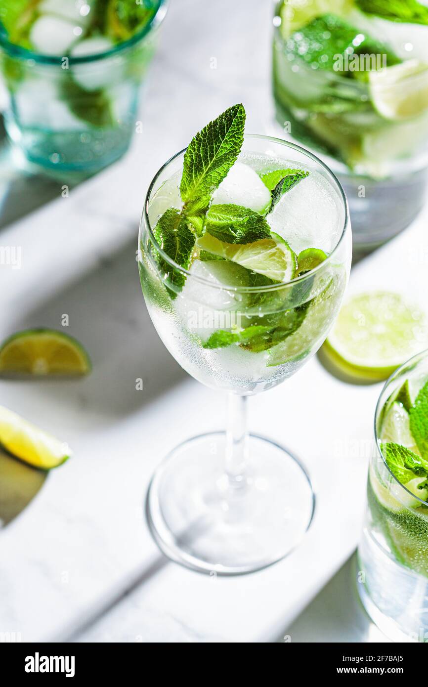 Cocktail Mojito con menta e lime in diversi bicchieri, sfondo in marmo bianco. Bevanda rinfrescante con lime e menta in bicchieri. Foto Stock