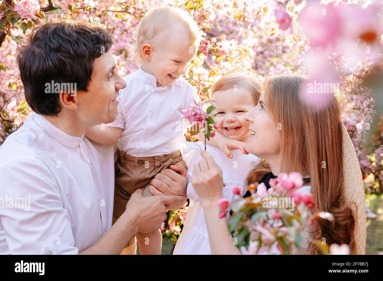 Genitori con figli, figlia e figlio sullo sfondo di un albero rosa fiorente sakura. Foto Stock