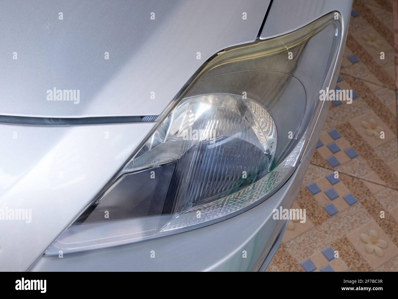 Il closeup del faro poco chiaro sulla piccola berlina è stato utilizzato per un lungo periodo in condizioni di clima caldo e umido, vista frontale con lo spazio di copia. Foto Stock