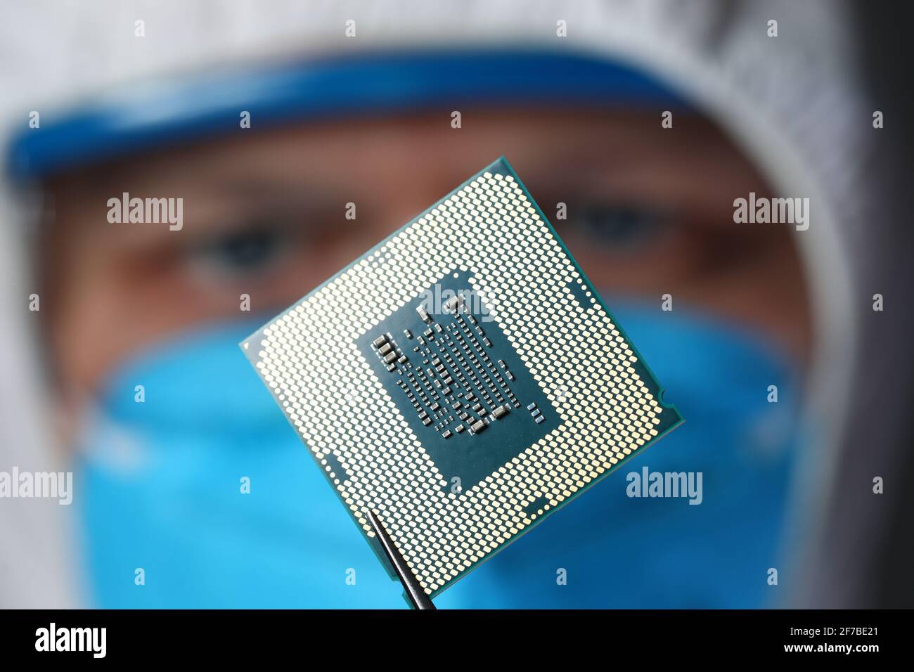 Lo scienziato mascherato tiene un microcircuito in forcipe Foto Stock