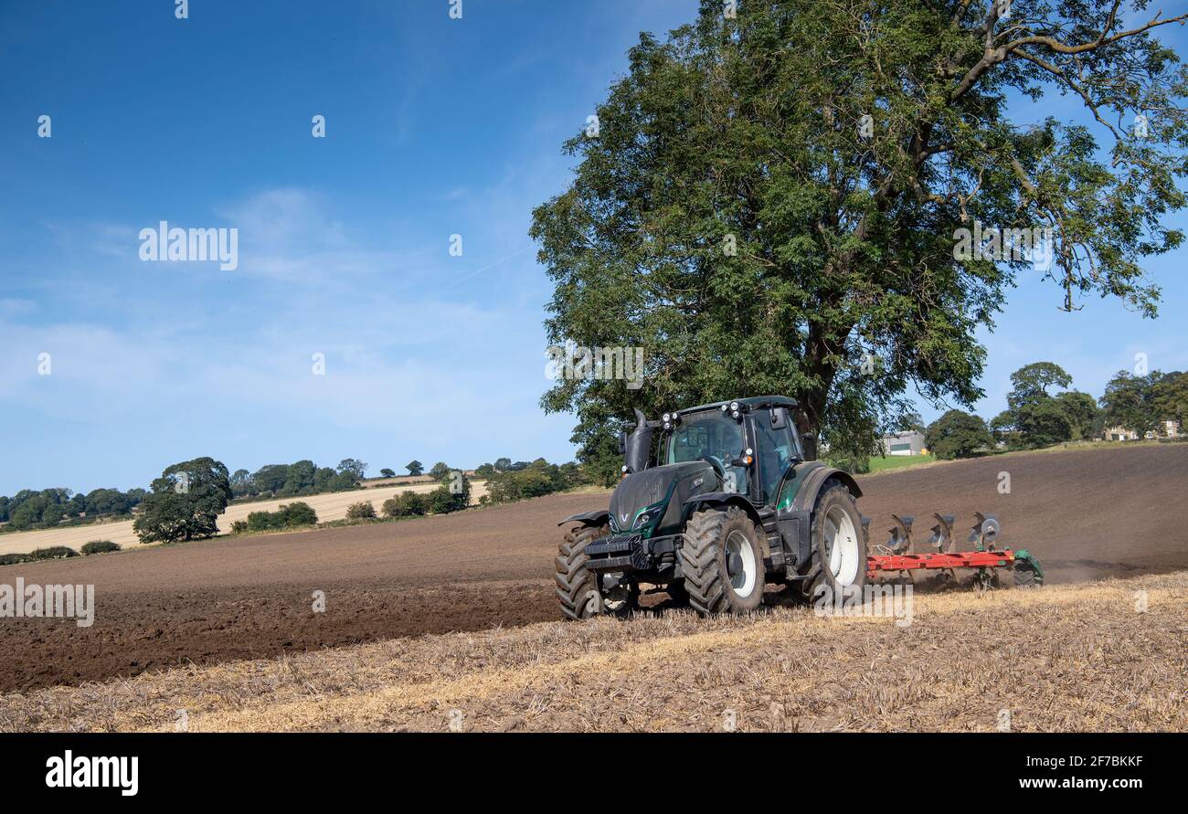 Aratura dell'agricoltore nelle stoppie dopo la raccolta del prodotto, utilizzando un trattore Valtra e un aratro a 5 solchi. North Yorkshire, Regno Unito. Foto Stock