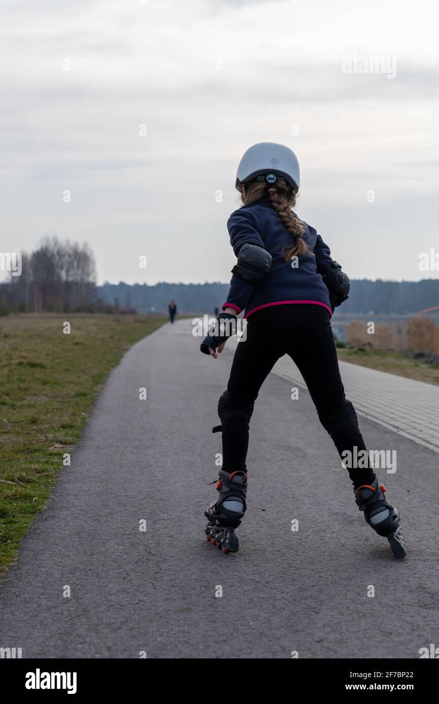 In linea che pattina all'esterno, una ragazza in un casco bianco vista posteriore. Sport all'aperto. Foto Stock