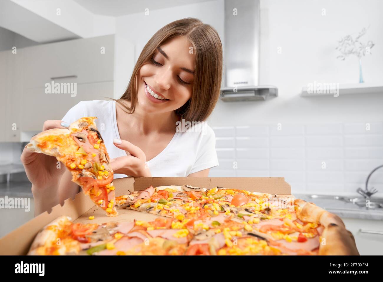 Primo piano di donna sorridente che tiene grande pizza e mangia pezzo a casa. Concetto di mangiare cibo gustoso a casa. Foto Stock