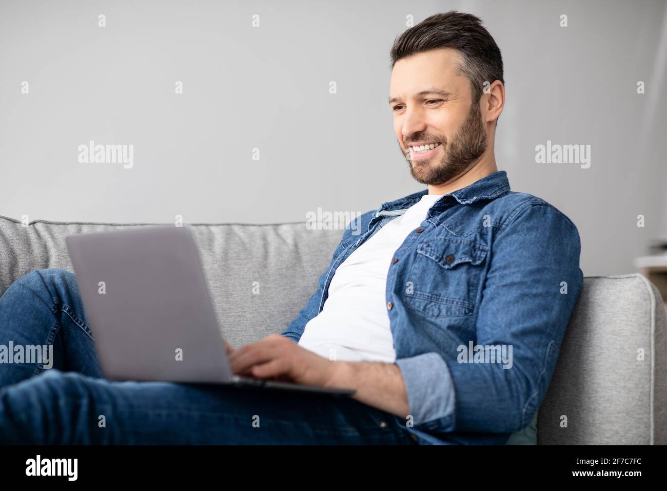 Uomo sorridente che usa il laptop, avendo un lavoro part-time a casa Foto Stock