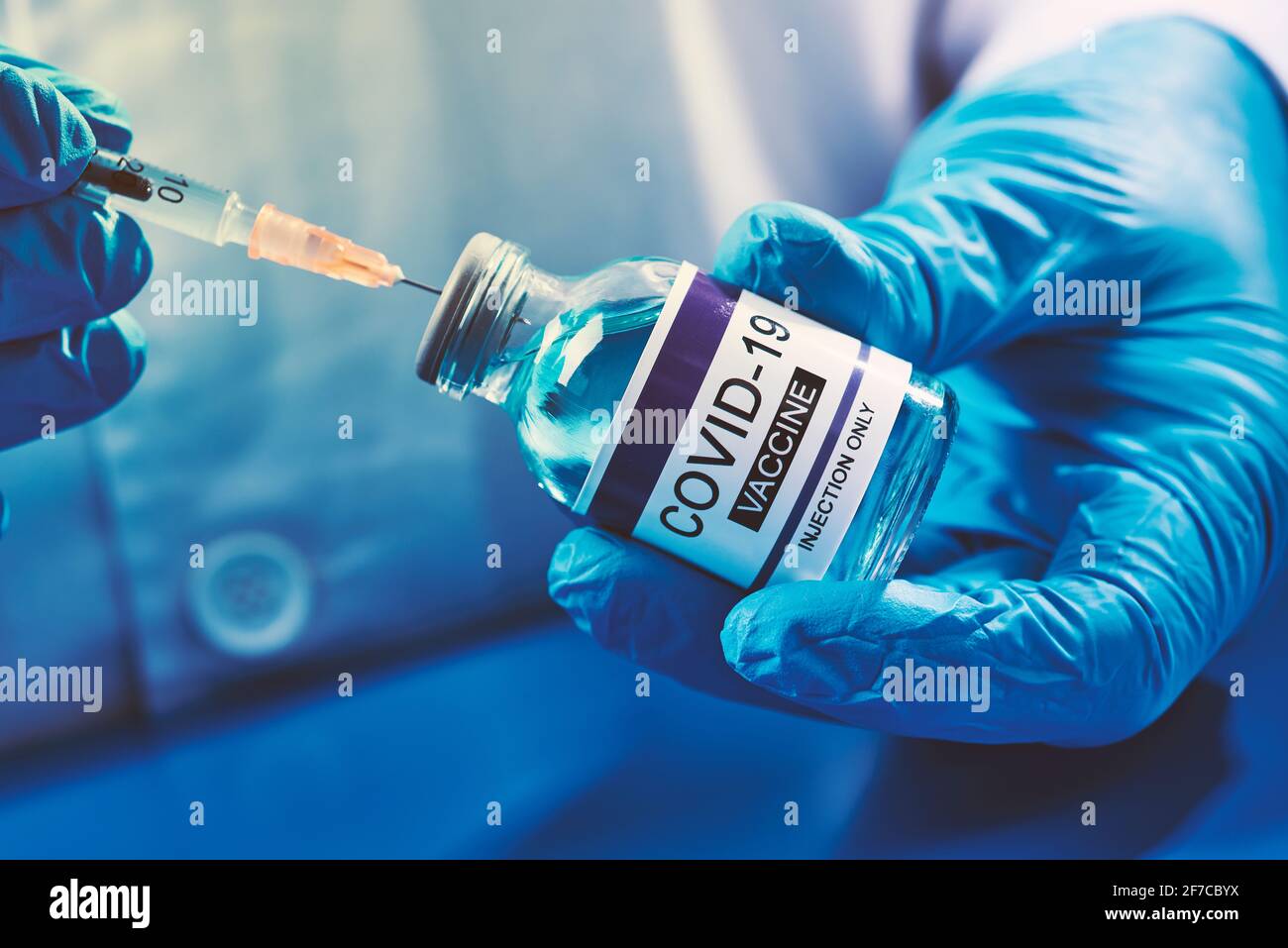 chiusura di un operatore sanitario, indossando guanti chirurgici blu, riempiendo una siringa da un flaconcino di un vaccino covid-19 simk Foto Stock