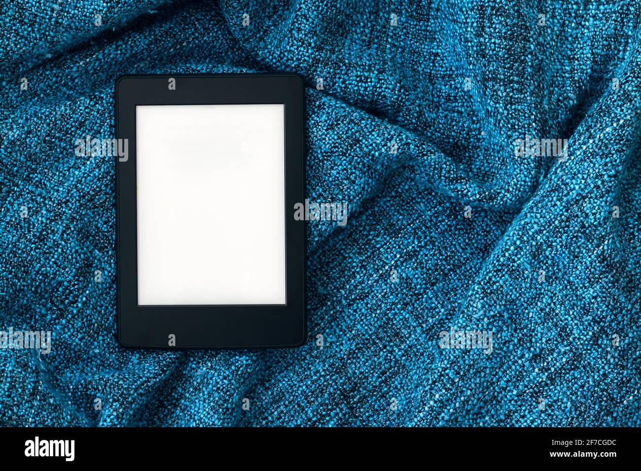 Un moderno libro elettronico nero con uno schermo vuoto su una coperta a maglia blu brillante. Tablet mockup. Vista dall'alto Foto Stock