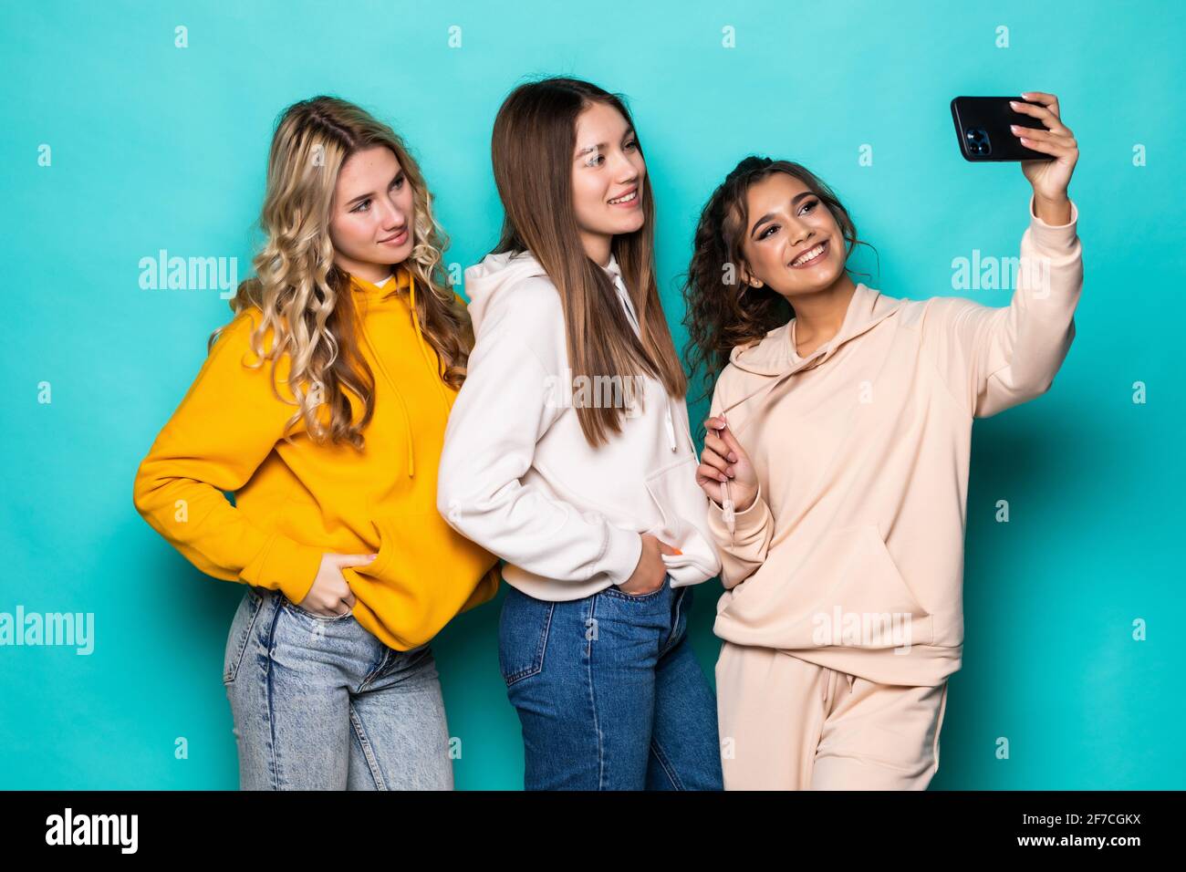 Giovani tre ragazze multietniche amici prendere un selfie da fotocamera posa su sfondo turchese Foto Stock