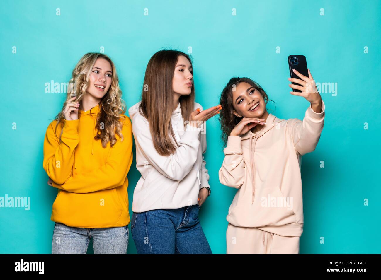 Giovani tre ragazze multietniche amici prendere un selfie da fotocamera posa su sfondo turchese Foto Stock