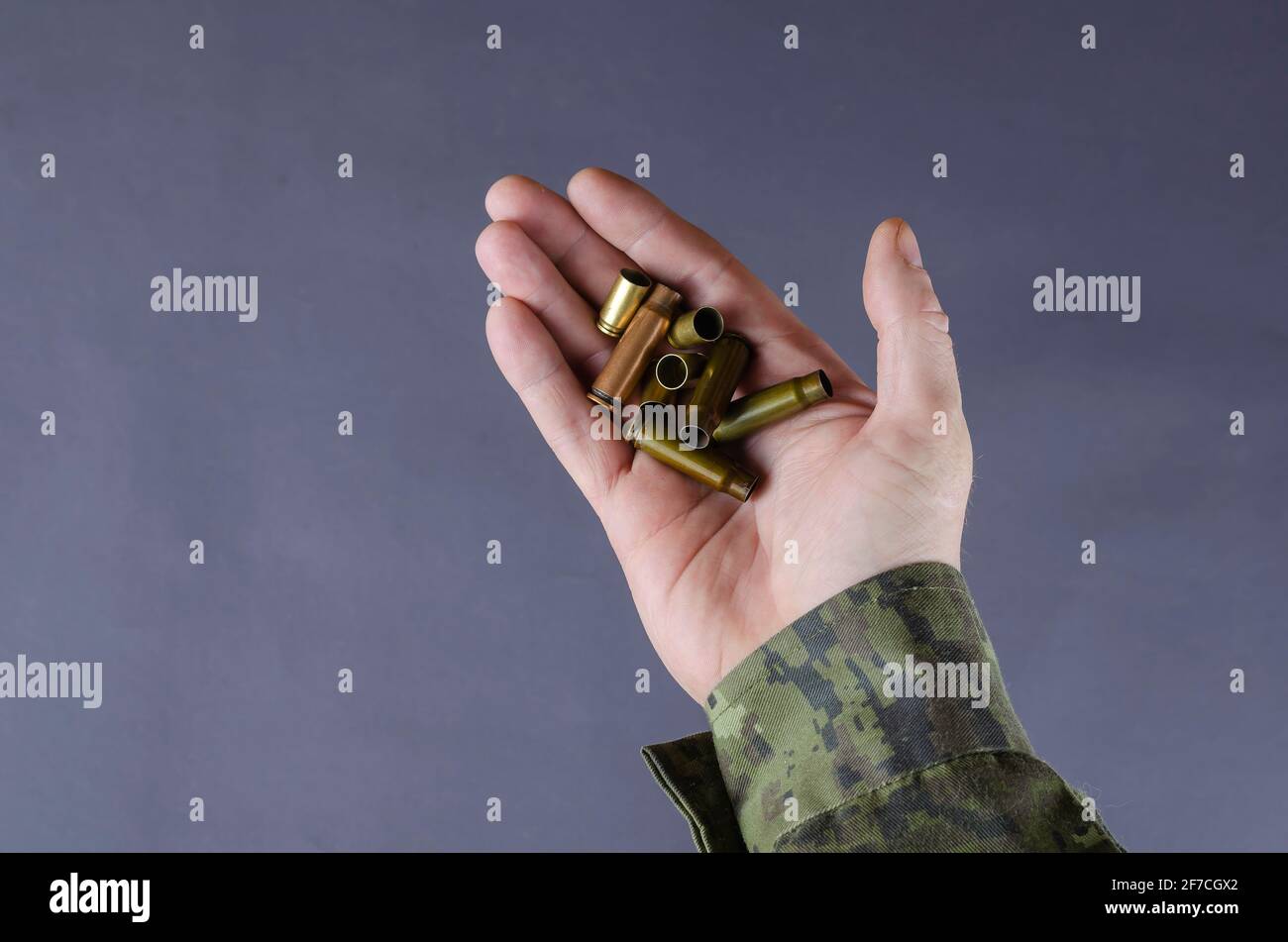 Involucri vuoti in una mano dell'uomo su uno sfondo grigio. Un uomo in una divisa camouflage sta tenendo in mano la pistola e i corpi della pistola della macchina secondaria. Tema dell'esercito. Milit Foto Stock