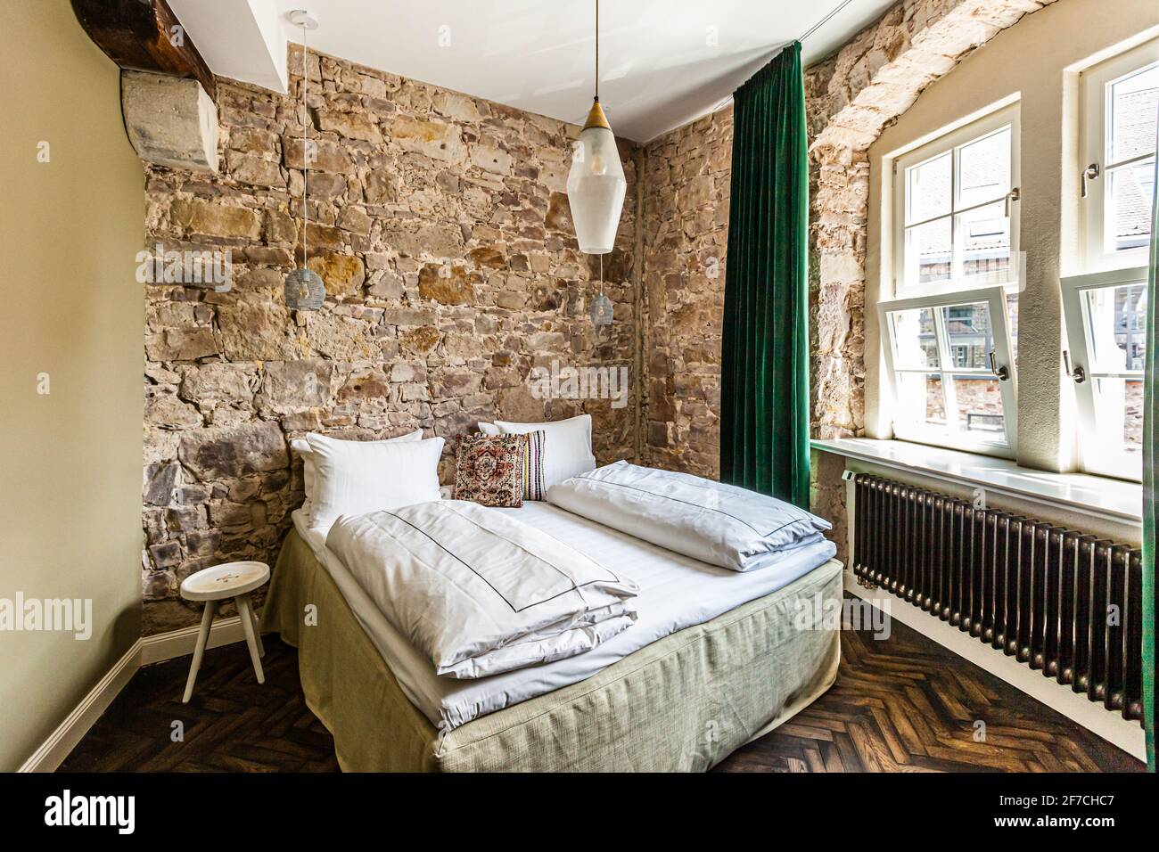 Una camera doppia con pareti in pietra naturale a vista e un letto Coco-Mat premium fa parte dell'Hotel Renthof a Kassel, Assia, Germania, un ex monastero carmelitano fondato nel 1298 e riaperto come hotel, ristorante e luogo per eventi nel giugno 2017, in coincidenza con la documenta 14. Materiali naturali – pietra, legno e una pesante tenda di velluto verde – definiscono l'interior semplice e sobrio della stanza. Foto Stock