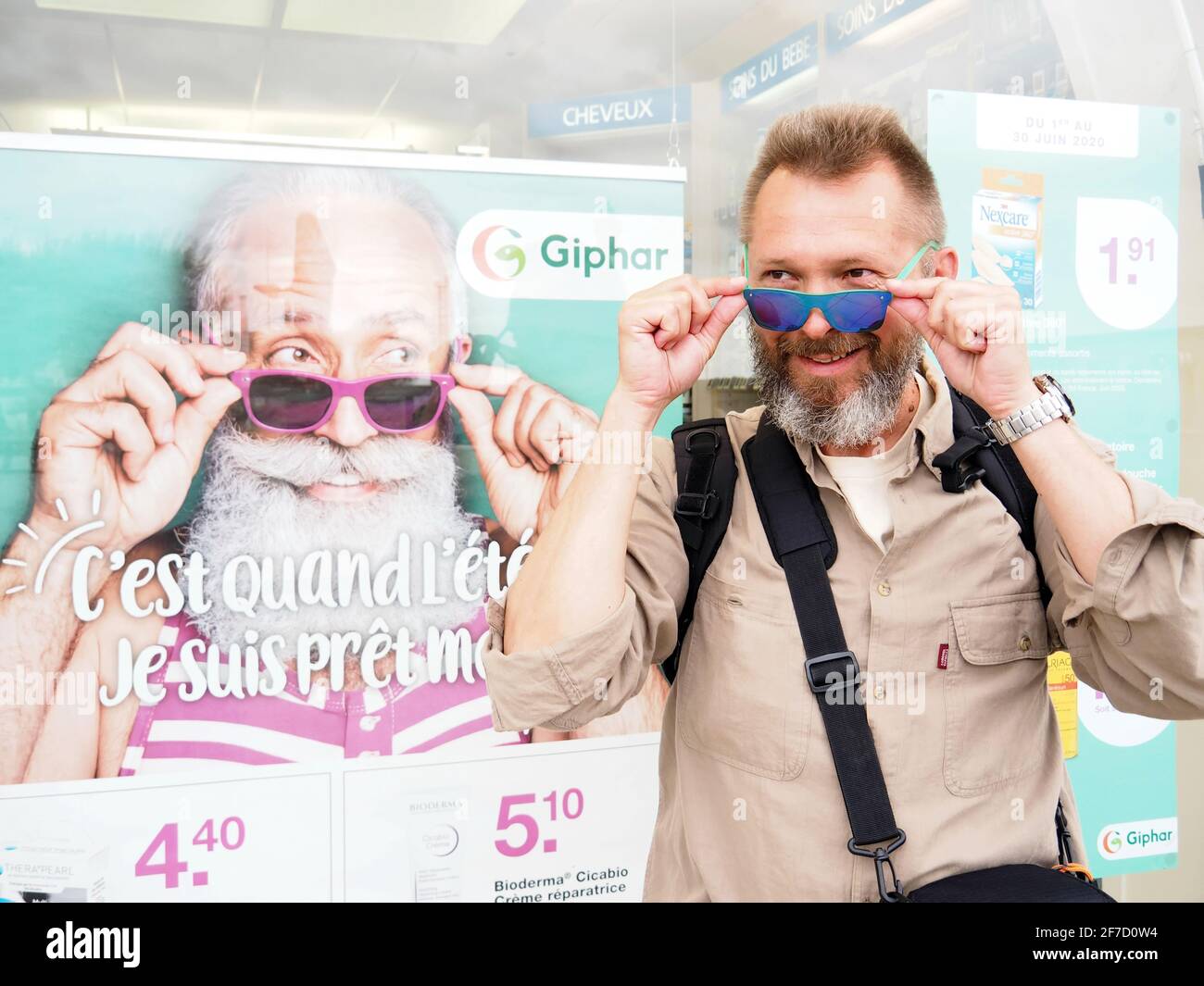 Uomo anziano in occhiali da sole su una pubblicità per la società  farmaceutica francese Gephar. Un uomo di mezza età in occhiali da sole si  trova vicino al poster Foto stock -