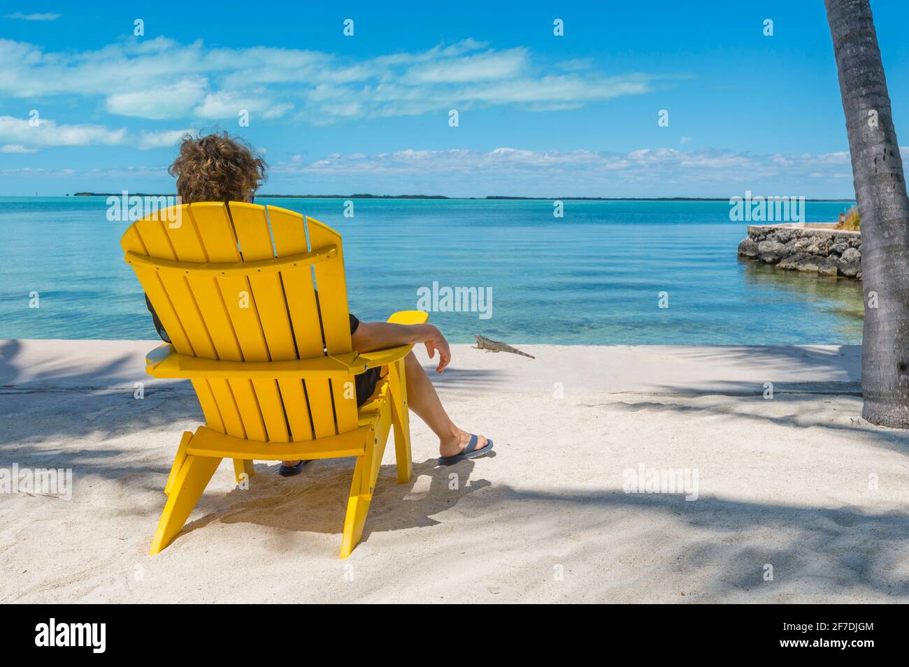 Donna seduta in giallo adirondack sedia, fissando contemplativamente fuori all'oceano caraibico in incredibilmente bella giornata di sole. Foto Stock