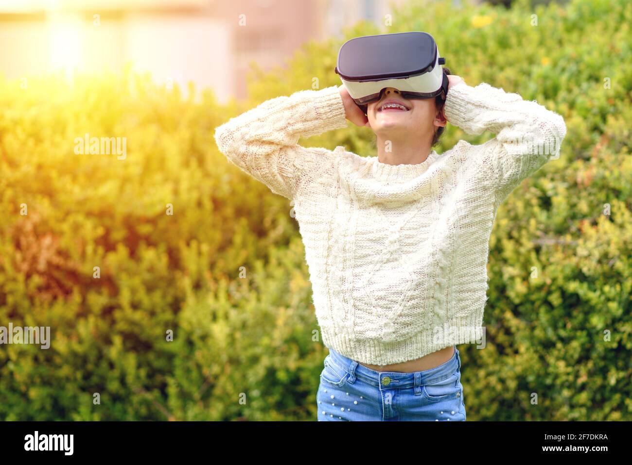Giovane bella ragazza adolescente sottile con tutore dentale che indossa occhiali di realtà virtuale in esterni natura sfondo. Smartphone con visore VR. Foto Stock