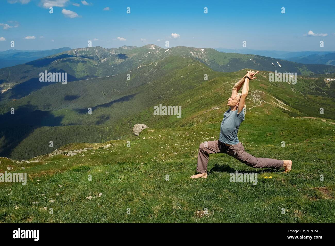 Uomo forte che pratica esercizi di yoga Balance in una giornata di sole sotto il cielo su una cima di montagna. Vacanze estive armonia all'aperto e vita sana Foto Stock