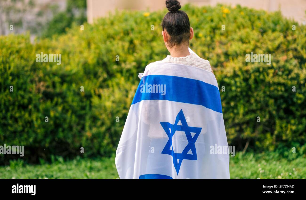 Ragazzina patriota ebrea in piedi con la bandiera di Israele avvolta intorno a lei. Memorial Day-Yom Hazikaron e Yom Ha'atzmaut concetto. Foto Stock