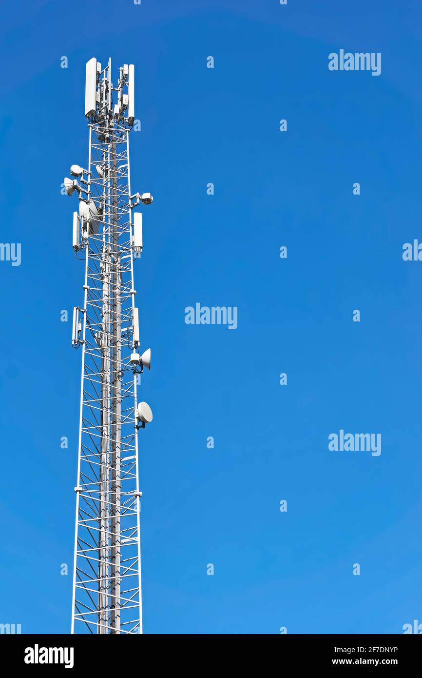 Trasmettitori 4G e 5G su una torre di telecomunicazioni. Stazione base cellulare con antenne di trasmissione bianche su un polo alto contro un cielo blu. Foto Stock