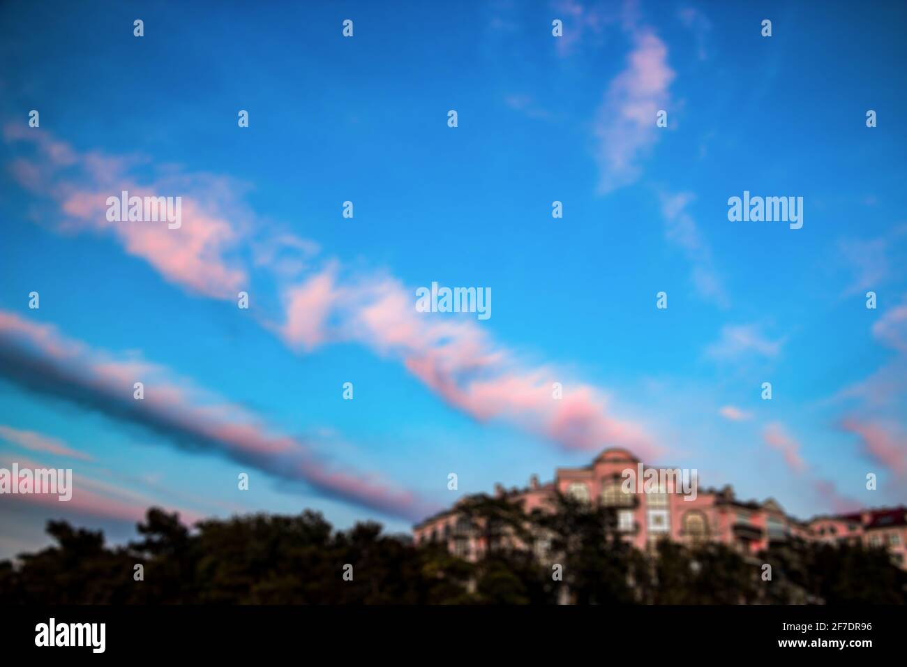 Nuvole rosa sfocate in un cielo blu ricco, accanto a un edificio dalle tonalità rosa. Paesaggio colorato al tramonto Foto Stock