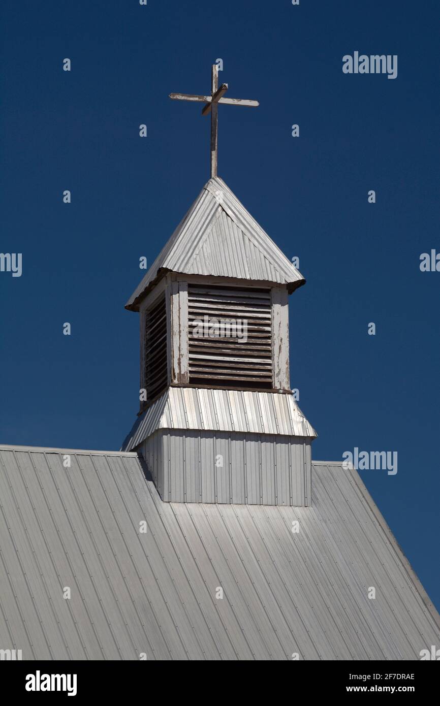 Una croce in cima a un campanile rustico su una chiesa con tetto di stagno nella campagna del New Mexico. Foto Stock