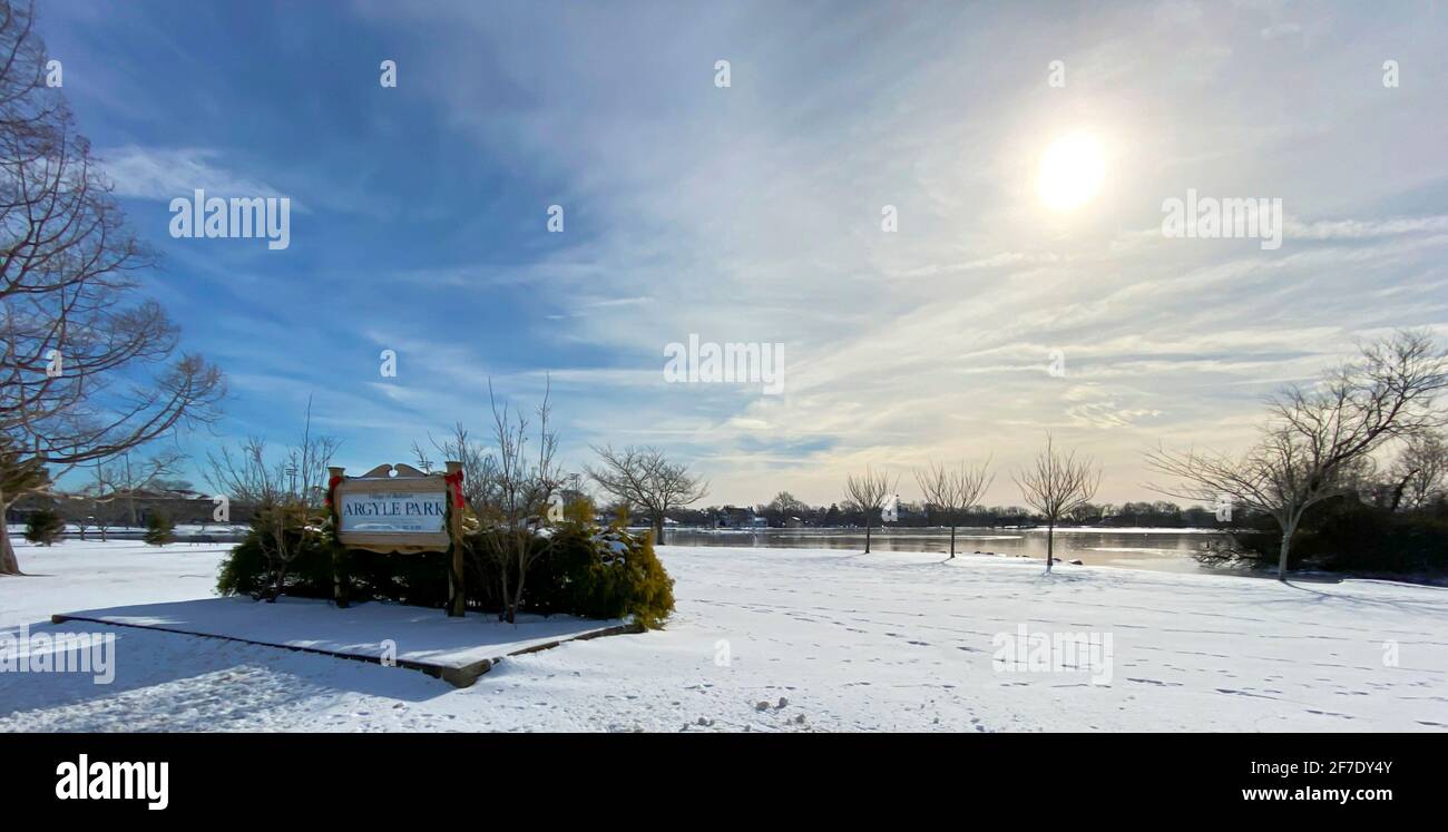 Vista orizzontale del lago del parco di Argyle nel villaggio di Babilonia coperto da una neve leggera con un bel paesaggio nuvoloso in cielo blu sopra. Foto Stock