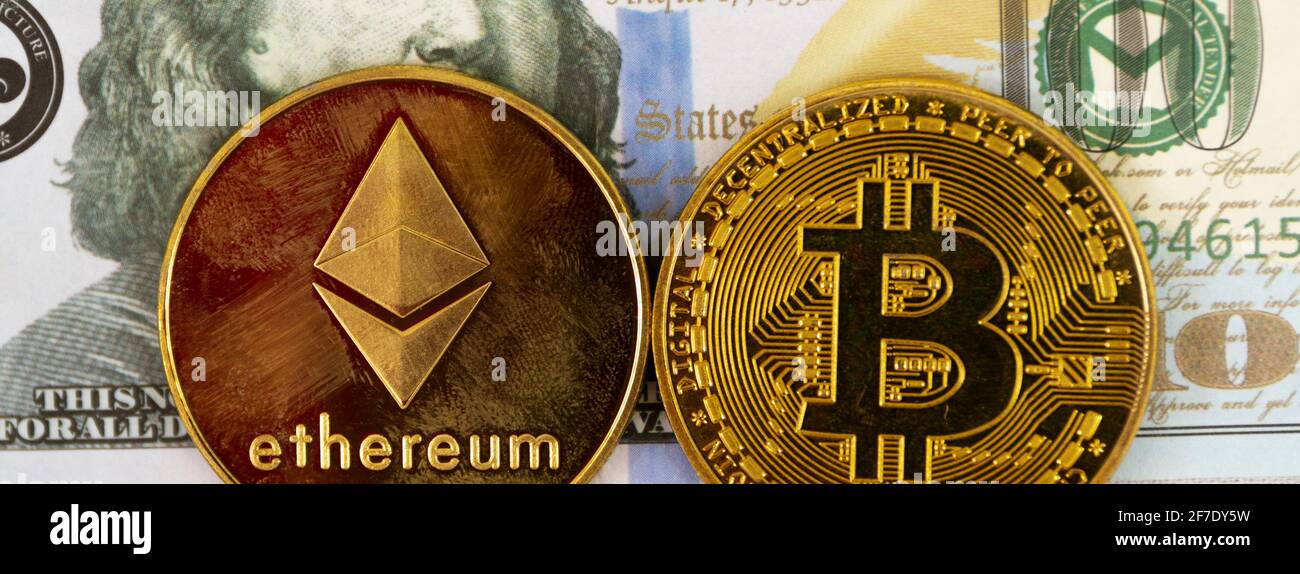 Un disegno di legge di cento dollari è lo sfondo per una moneta d'oro di Ethereum e una moneta di bit. Foto Stock