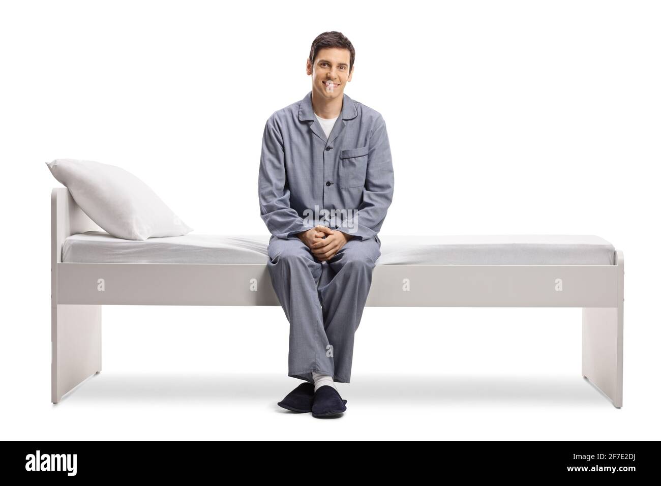 Sorridente giovane in pigiama seduto su un letto isolato su sfondo bianco Foto Stock