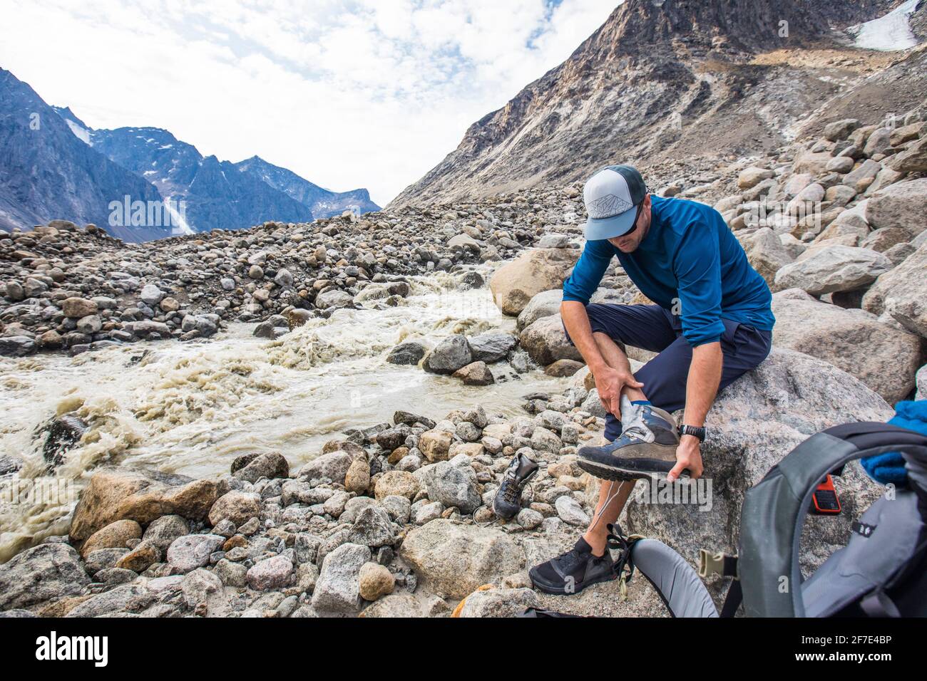 Backpacker cambia le calzature per attraversare il fiume. Foto Stock