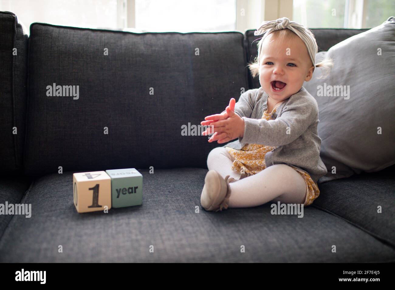 Una ragazza di un anno seduta sul divano che si aggrappava con eccitazione Foto Stock