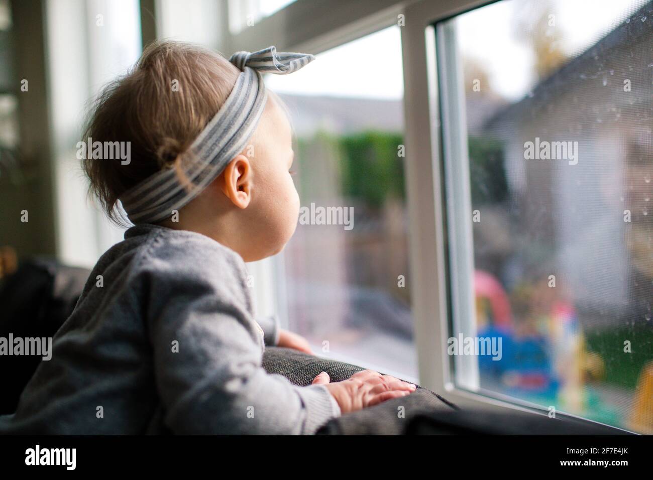 vista laterale di giovane ragazza che guarda fuori la finestra nel suo cortile. Foto Stock