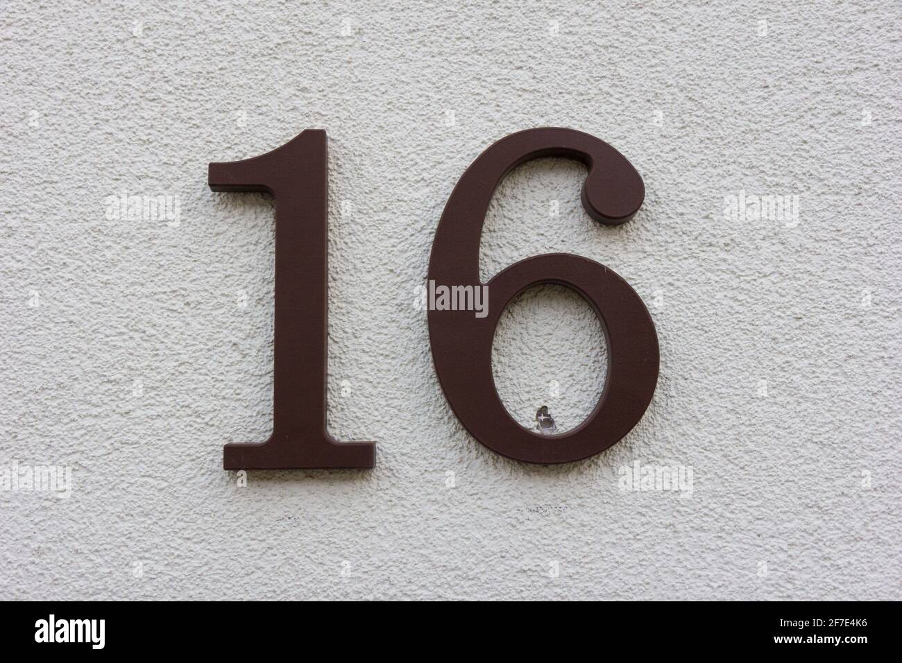 Numero 16 in plastica marrone su una parete bianca in gesso Foto Stock Numero 16 in plastica marrone su una parete bianca in gesso Foto Stock