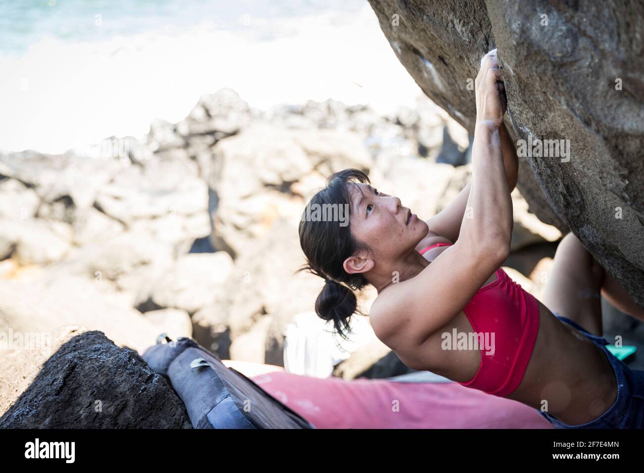 Giovane donna asiatica che arrampica sapientemente una roccia sulla spiaggia In o'ahu Foto Stock