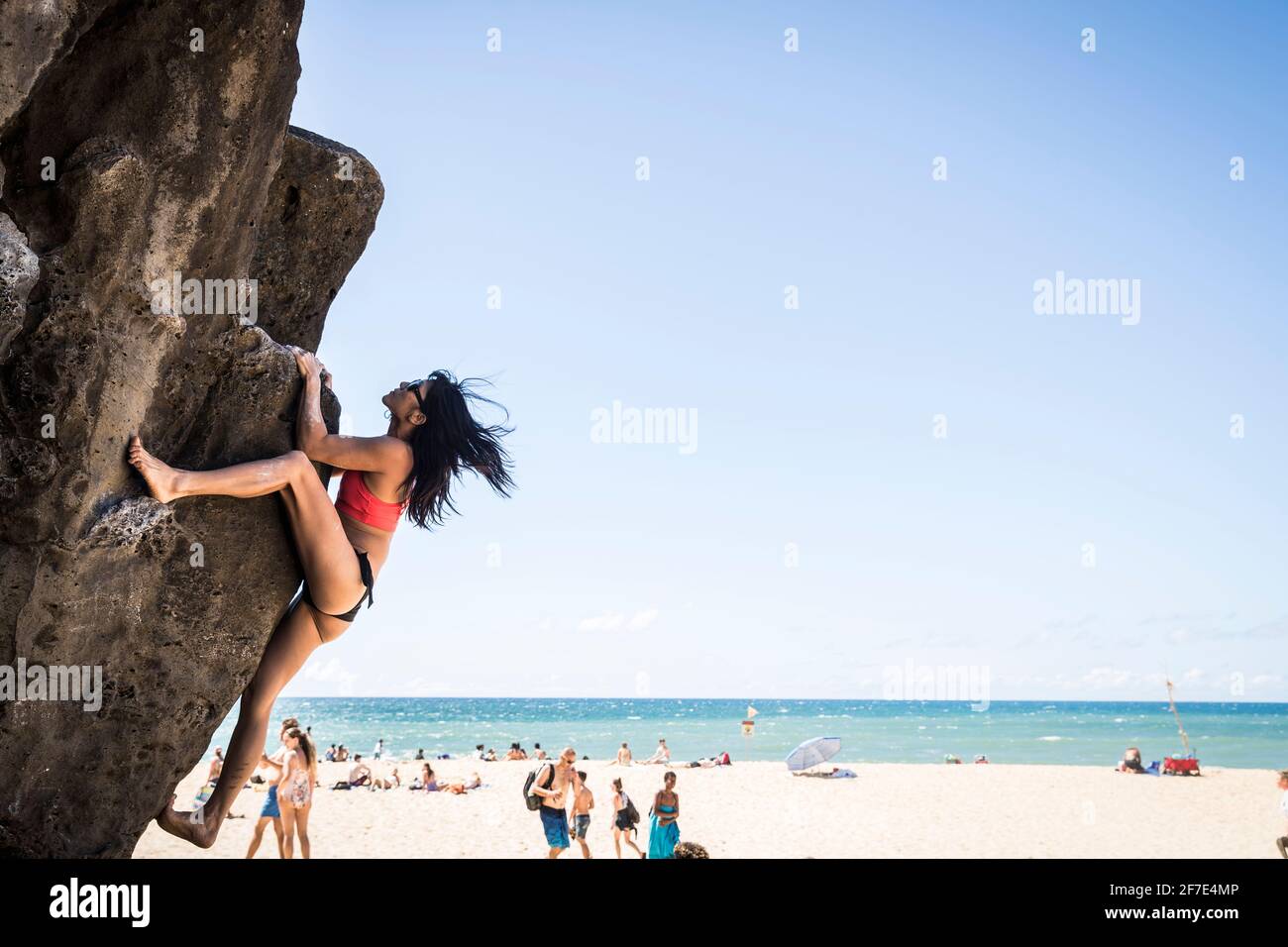 Donna bruna in bikini che arrampica una roccia in spiaggia in una giornata di sole Foto Stock