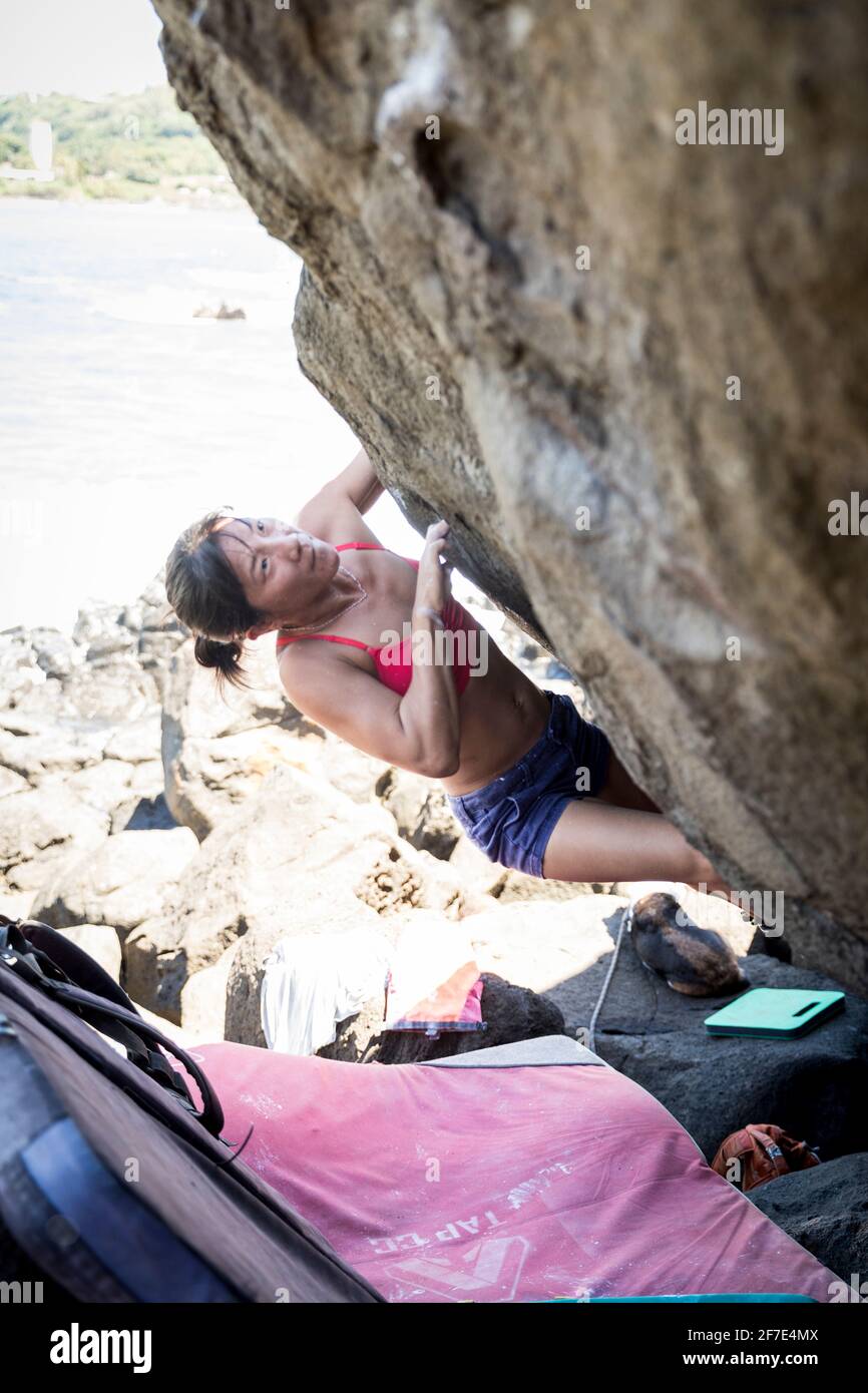 Donna concentrata che prende una pausa dalla spiaggia per salire una roccia Foto Stock
